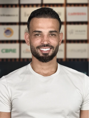 Andrew Raso, founder of Online Marketing Gurus, smiling in a white t-shirt in front of the OMG client logo wall.