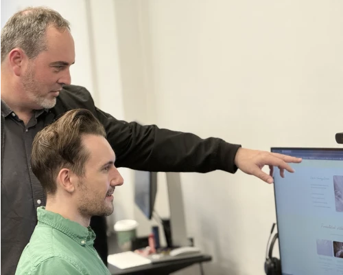 Two Online Marketing Gurus designers reviewing a website design on screen together, with one pointing out details on the monitor.