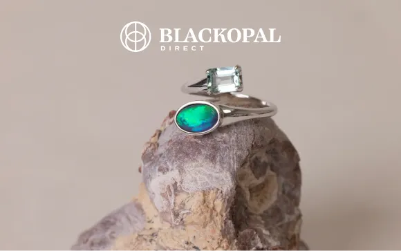 Blackopal Direct logo above a silver ring with a green and blue opal and a pale green gemstone on a rock.